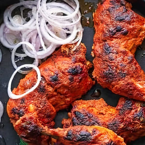 Close-up of Bawarchi Biryanis' Indian tandoori chicken, charred and red, with white onion rings.