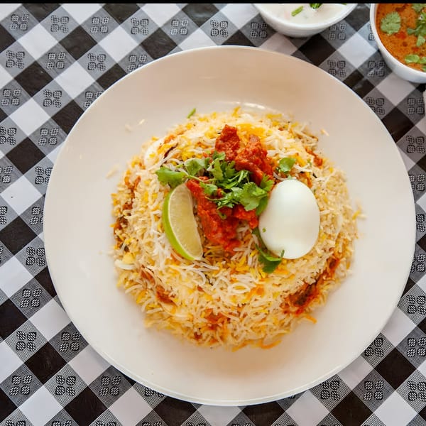 Bawarchi Biryanis' chicken biryani with a boiled egg, lime, and cilantro on a white plate.