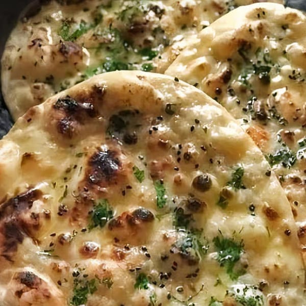 Close-up of three pieces of garlic naan bread, garnished with herbs and black sesame seeds.