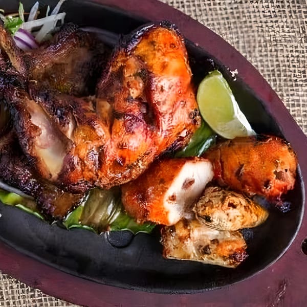 Bawarchi Biryanis' Tandoori Chicken, a vibrant red-orange dish with lime and onions on a dark platter.