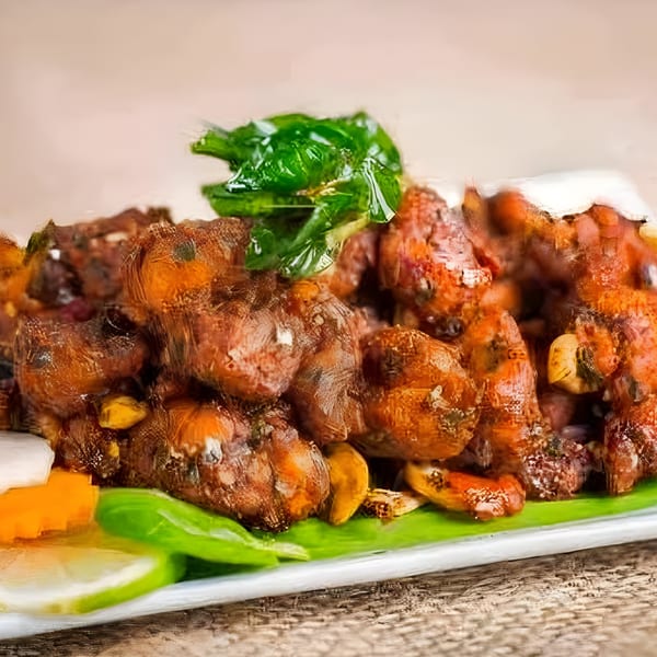 Close-up of Bawarchi Biryanis' Indian chicken dish, garnished with green leaves, cashews, and lemon.