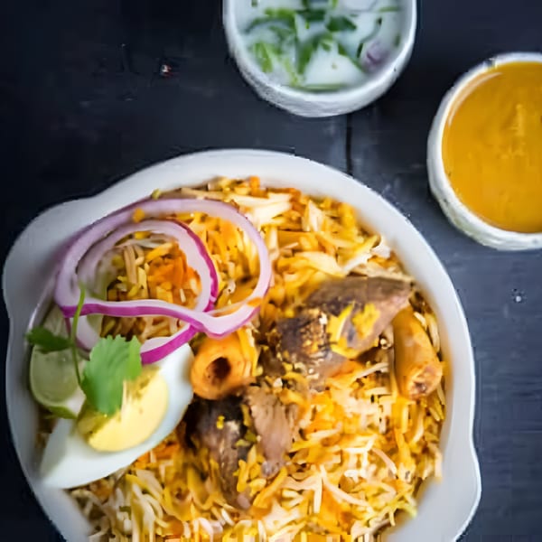 Bawarchi Biryanis' Mutton Biryani, garnished with red onions, egg, and cilantro, with raita and curry.